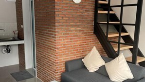 A modern living room with a brick accent wall, a grey sofa with cushions, a white coffee table, and a staircase with wooden steps. - Sealoft,Pattaya (Pattaya)