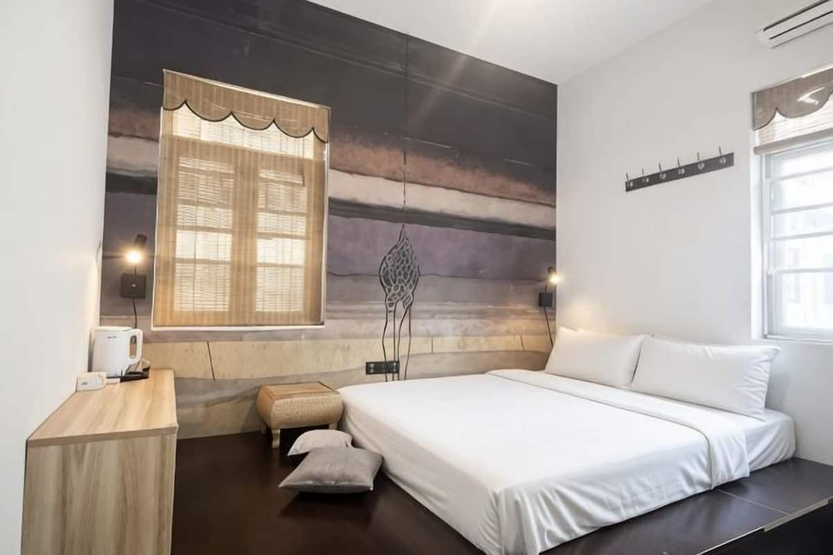 A bedroom with a bed, bedside table, lamp, window, and wall-mounted shelf.