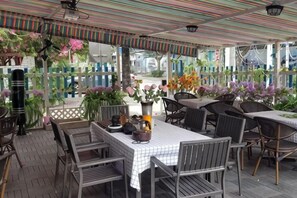 An outdoor patio with tables and chairs, surrounded by potted plants and flowers.