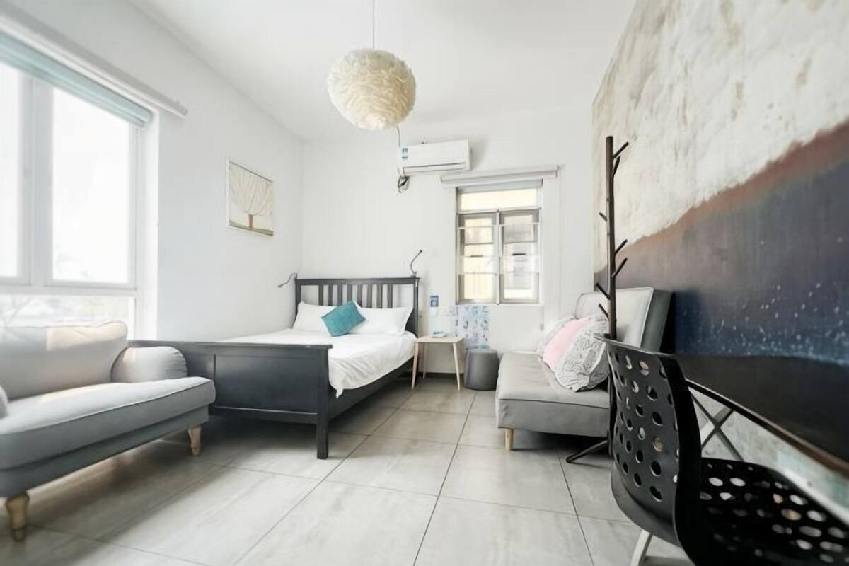 A modern bedroom with a bed, a sofa, a desk, and a large painting.