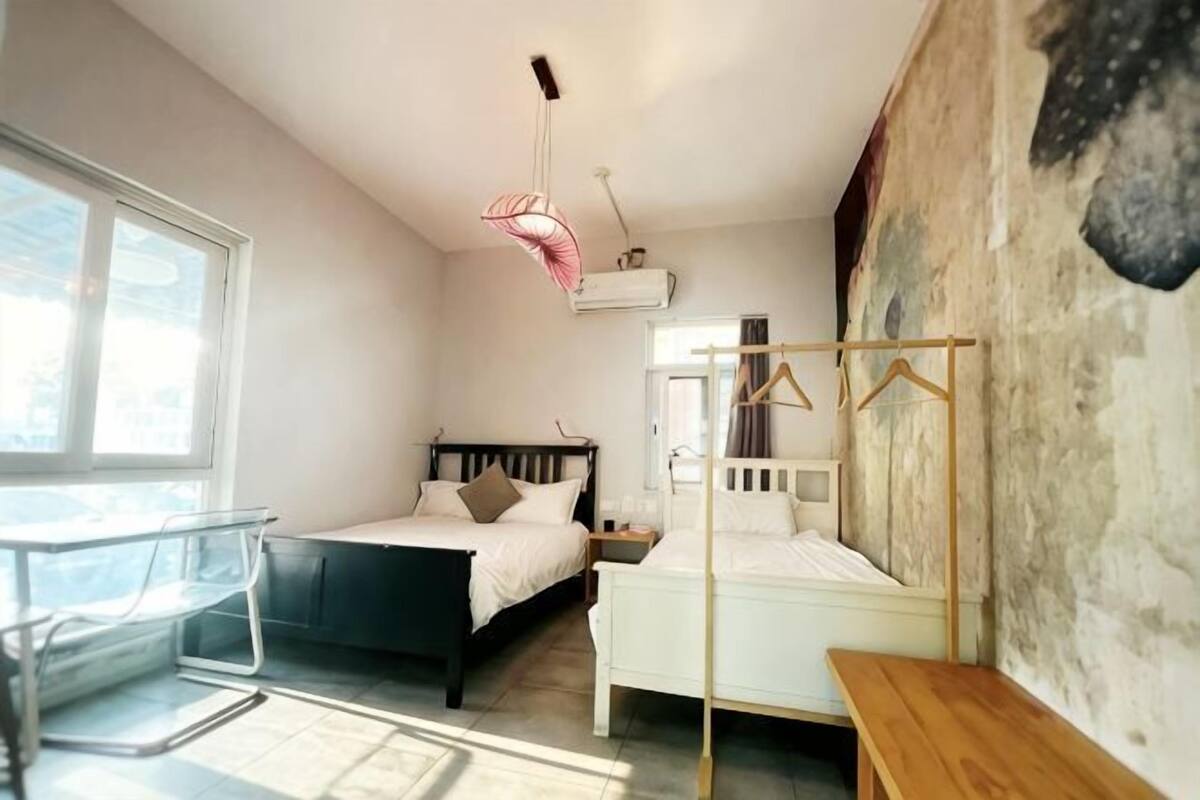 A bedroom with two beds, a chair, a bedside table, a hanging light, and a window.