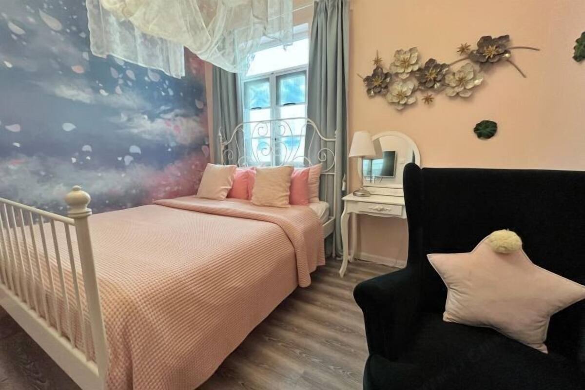 A bedroom with a bed, a desk, a chair, and a wall with decorative elements.