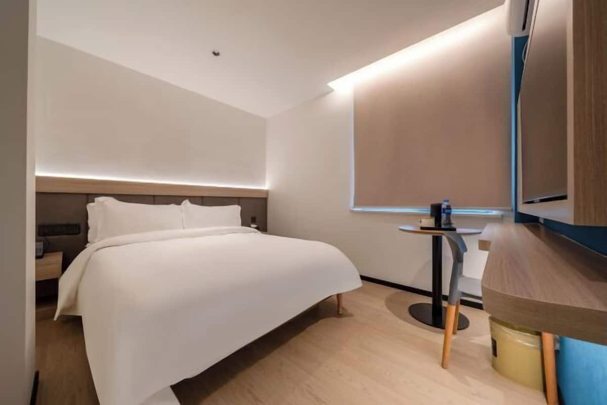 A modern hotel room with a bed, bedside table, and a small desk with a chair.