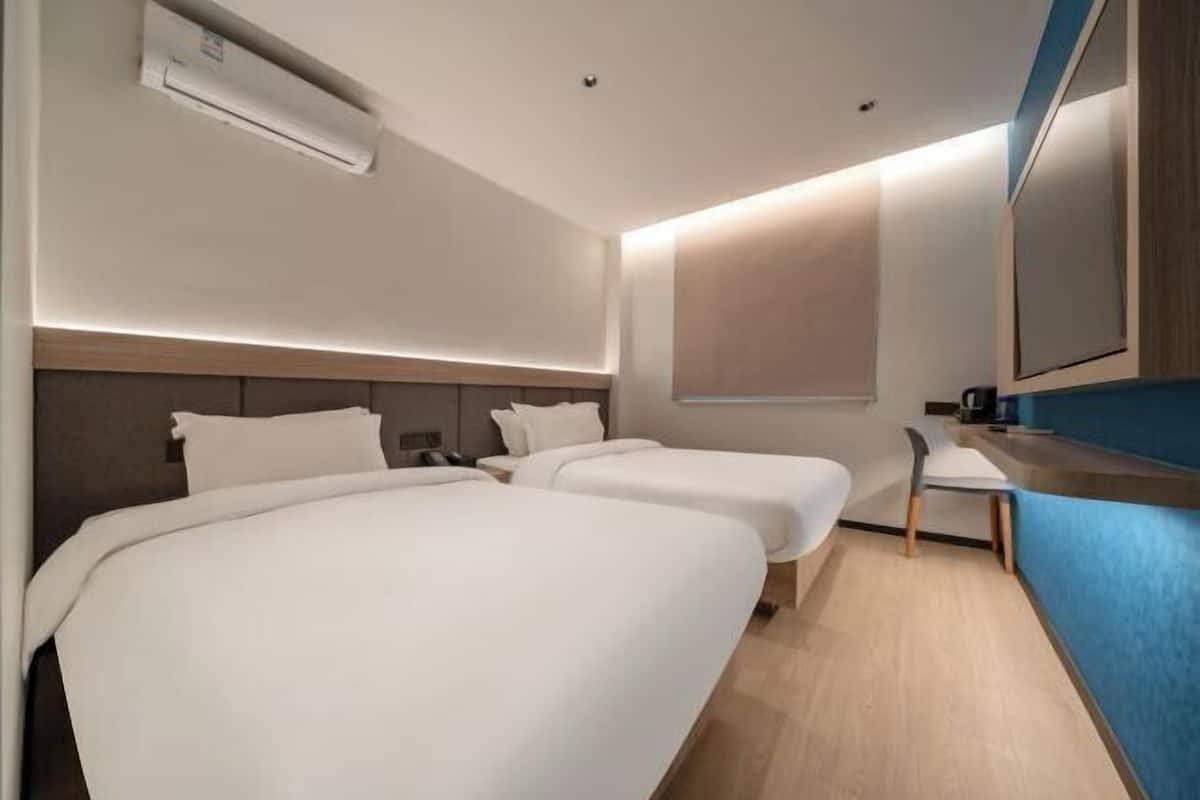 A hotel room with two beds, a desk, a chair, a mirror, and a window.