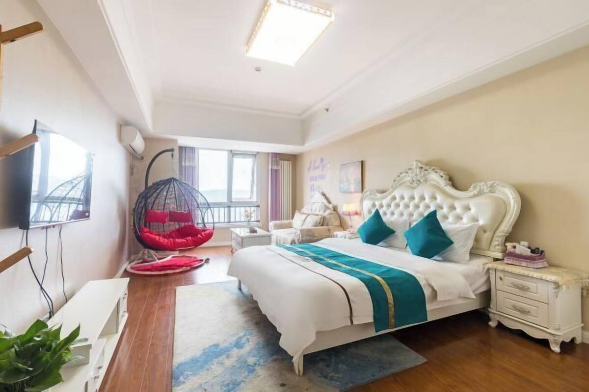 Une chambre avec un grand lit, un fauteuil suspendu, une table de chevet et un téléviseur fixé au mur.