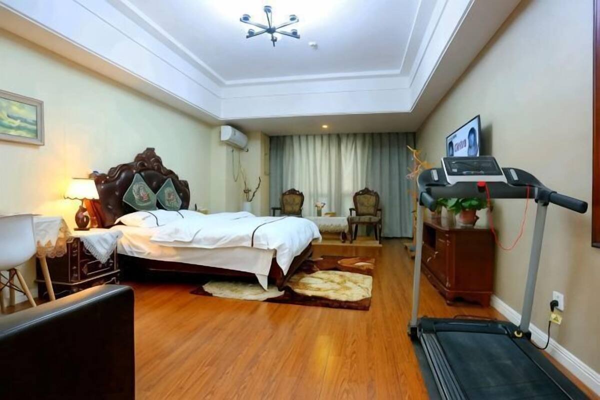 Une chambre d’hôtel équipée d’un lit, d’une table de chevet, d’une lampe, d’une chaise, d’un tapis de course et d’un téléviseur fixé au mur.