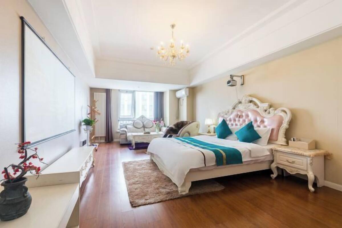Une chambre à coucher avec un grand lit, un lustre, une table de chevet et une fenêtre avec des rideaux.
