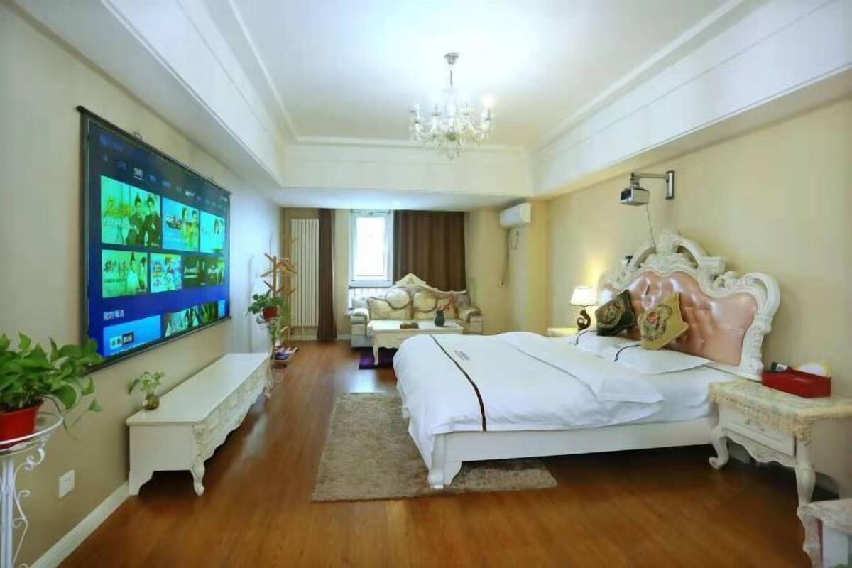Une chambre d’hôtel dotée d’un grand téléviseur à écran plat fixé au mur, d’un lit avec une tête de lit décorative, d’une table de chevet et d’un banc le long du mur.