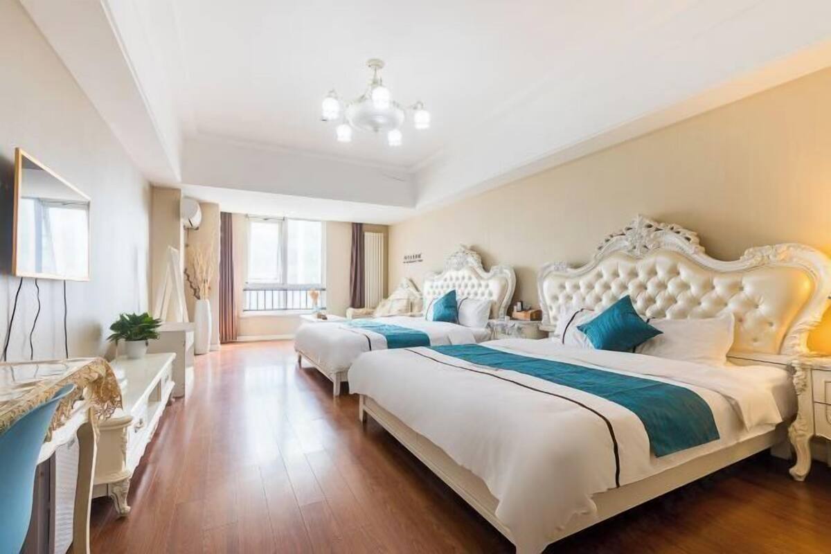 Une chambre d’hôtel avec deux lits, un lustre, une commode et une grande fenêtre.