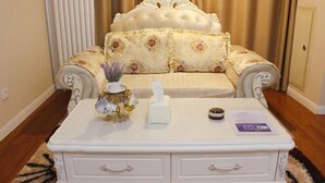 Ein Zimmer mit einem weißen, gepolsterten Sofa mit Blumenmuster, einem weißen Nachttisch mit Schubladen und einer dekorativen Vase.