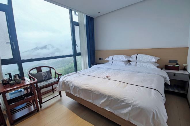 Habitación de hotel con una cama grande, un escritorio de madera y vistas a las montañas a través de amplias ventanas.