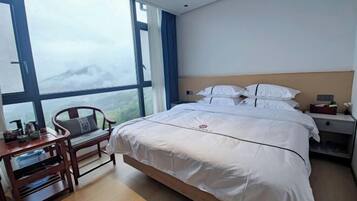 Habitación de hotel con una cama grande, un escritorio de madera y vistas a las montañas a través de amplias ventanas.