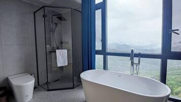 Un baño moderno con una bañera independiente, ducha con cerramiento de vidrio y vistas a un paisaje montañoso a través de amplias ventanas.