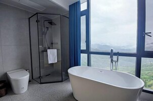 A modern bathroom with a freestanding bathtub, a glass-enclosed shower, and a view of a mountainous landscape through large windows.