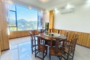 Un comedor con una mesa redonda y sillas, ventanas amplias con vista a la montaña y un equipo de aire acondicionado en la pared.