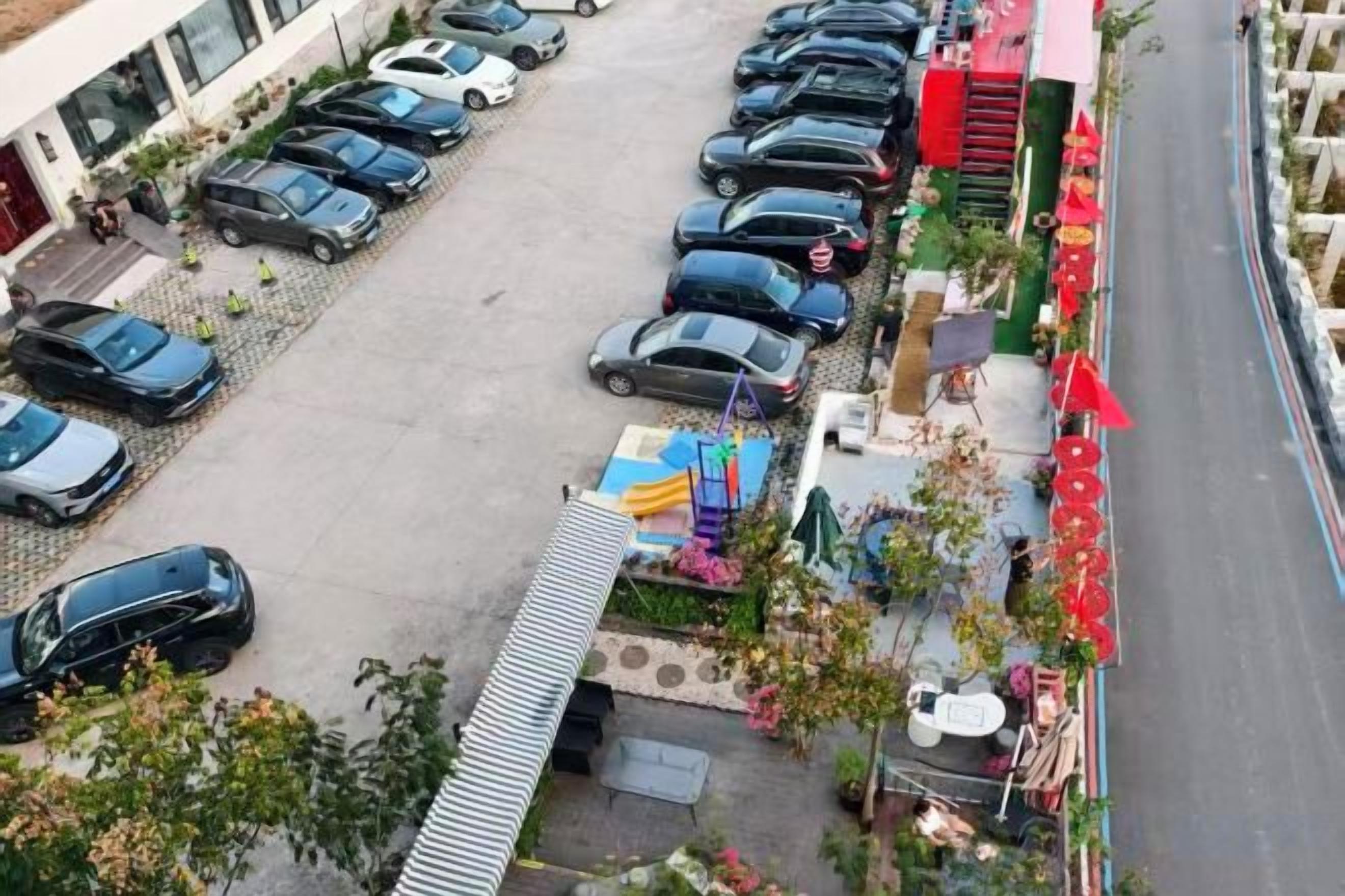 Ein Parkplatz mit mehreren Autos, eine kleine Außenbereich-Sitzgelegenheit mit Tischen und Stühlen sowie ein Gebäude mit Flachdach im Hintergrund.
