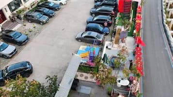 Ein Parkplatz mit mehreren Autos, eine kleine Außenbereich-Sitzgelegenheit mit Tischen und Stühlen sowie ein Gebäude mit Flachdach im Hintergrund.