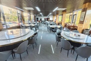 Un amplio comedor interior con mesas y sillas redondas, ventanas grandes y un diseño de techo moderno.