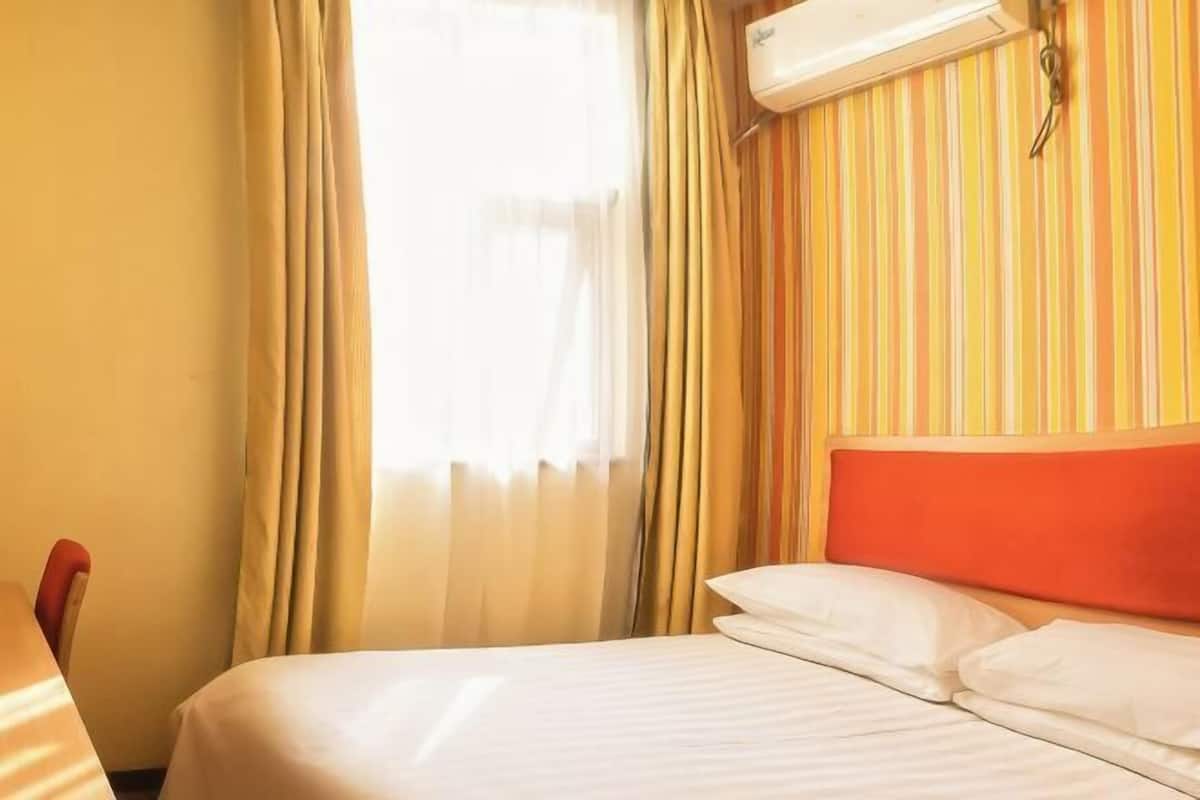 A hotel room with a bed, curtains, and an air conditioning unit.