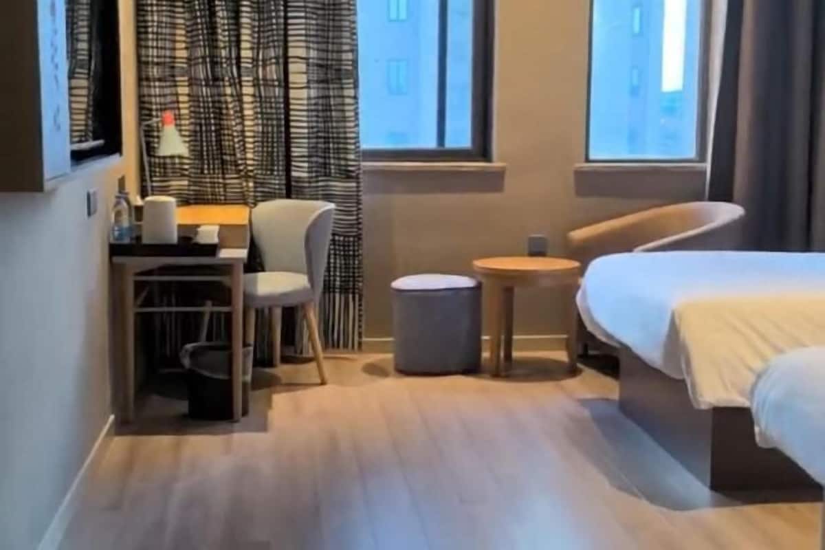 A compact hotel room with a bed, a desk with a chair, a small round table, and a window with curtains.