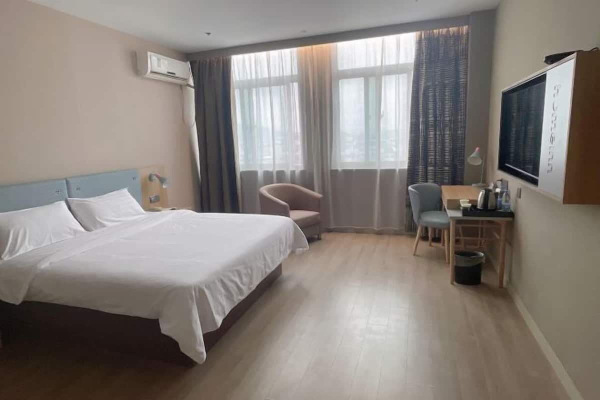A hotel room with a large bed, a desk with a chair, a TV, and a window with curtains.
