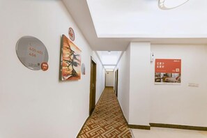 Un couloir d’hôtel avec un tapis à motifs, une horloge et des affiches d’information accrochées aux murs.