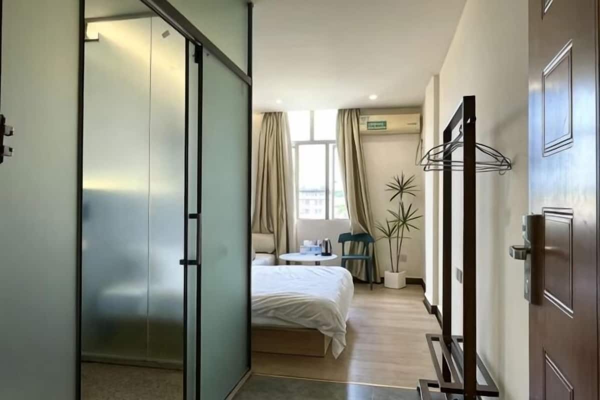 Ein Hotelzimmer mit Bett, Schreibtisch, Stuhl, einer Zimmerpflanze und einer Schiebetür.