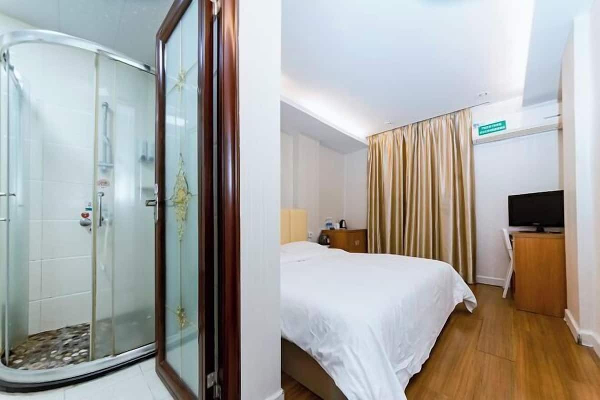 Ein Hotelzimmer mit einer Duschkabine aus Glas, einem Bett mit weißer Bettwäsche, einem Holztisch und einem Fernseher.