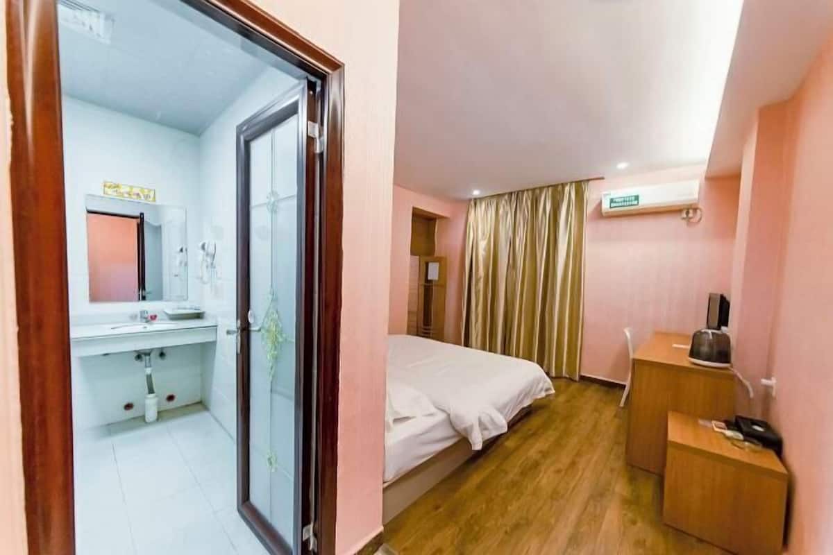 Ein Hotelzimmer mit Bett, Schreibtisch, Spiegel, Waschbecken und Klimaanlage.