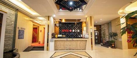 A hotel lobby with a reception desk, a patterned wall, and a geometric floor design.