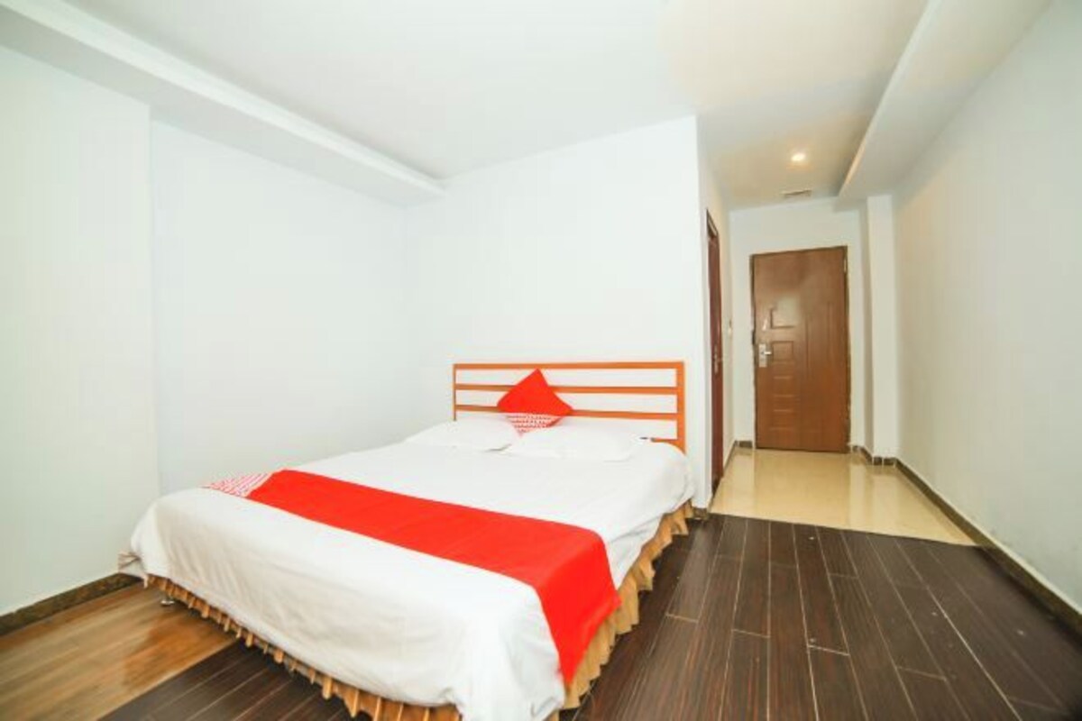 A single bed with a wooden headboard, white bedding, and a red accent.