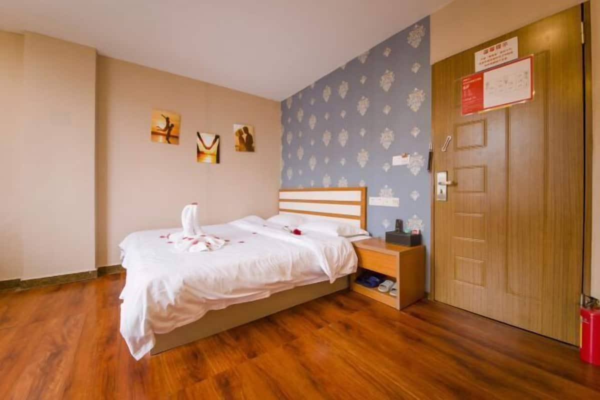 Ein Hotelzimmer mit Bett, Holzboden, einem Nachttisch, einer Wand mit floralem Muster und einer Tür mit einem Schild.