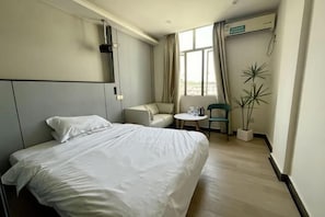 Una habitación de hotel con una cama, una mesita pequeña, una silla y una planta en maceta.