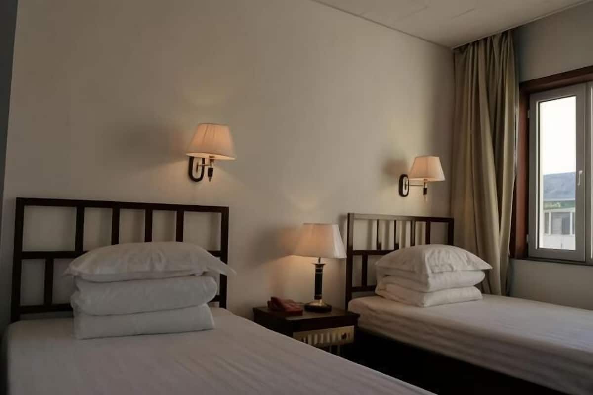 Ein Hotelzimmer mit zwei Einzelbetten, Nachttischlampen, einem Nachttisch und einem Fenster mit Vorhängen.