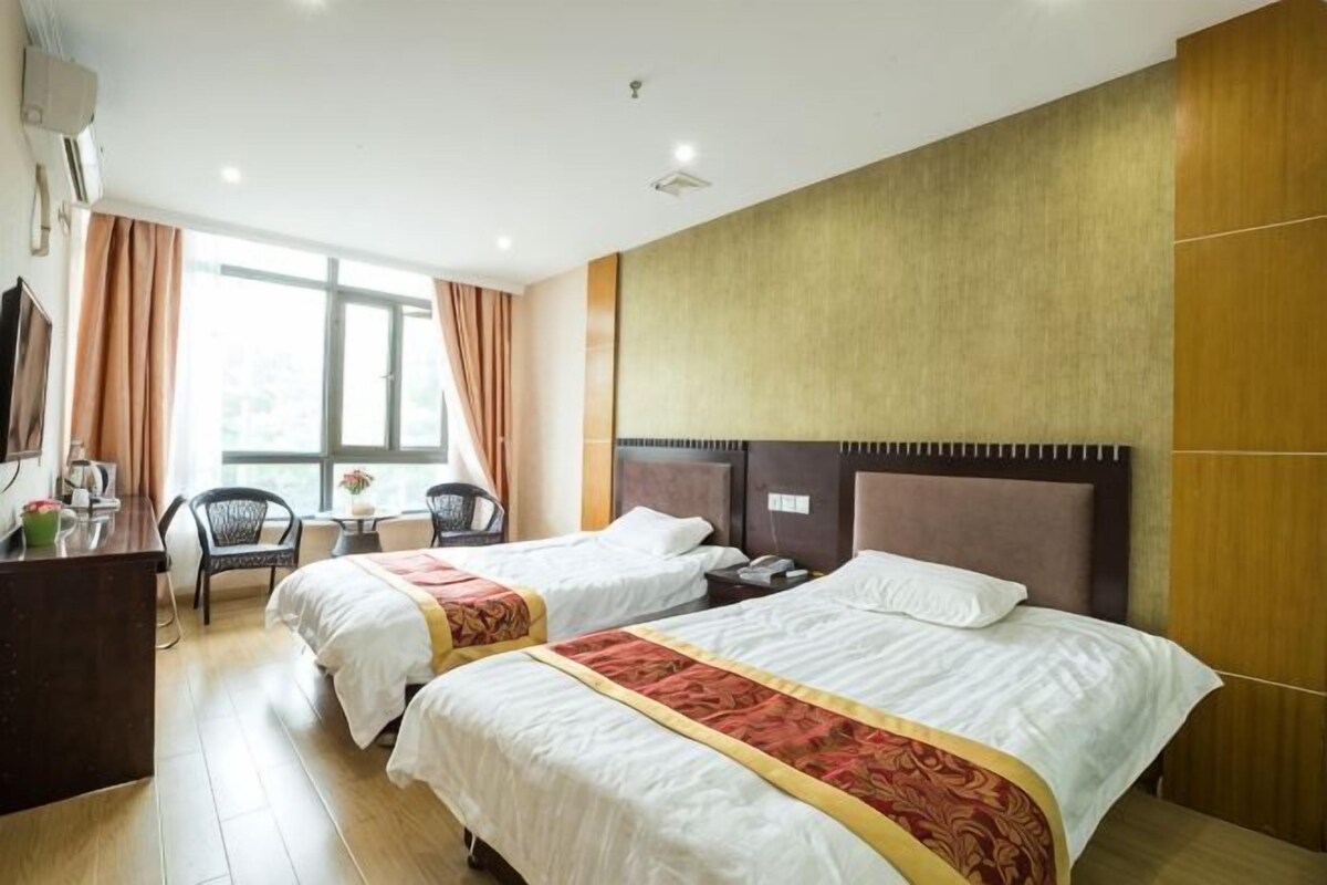 A hotel room with two beds, a desk, a chair, and a television.