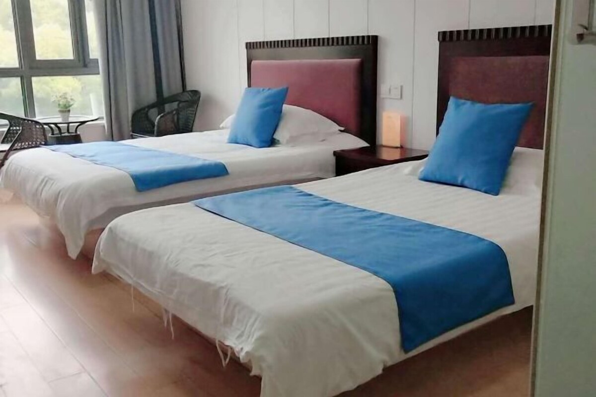 A hotel room with two beds, each with a blue and white bedspread, and a small table with a chair.