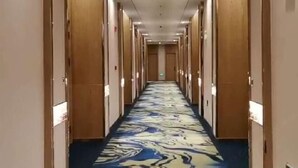 Ein Hotelgang mit Teppichmuster, Holztüren und Deckenleuchten.