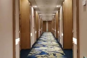 Pasillo de hotel con puertas a ambos lados, alfombra estampada y pared de color claro.
