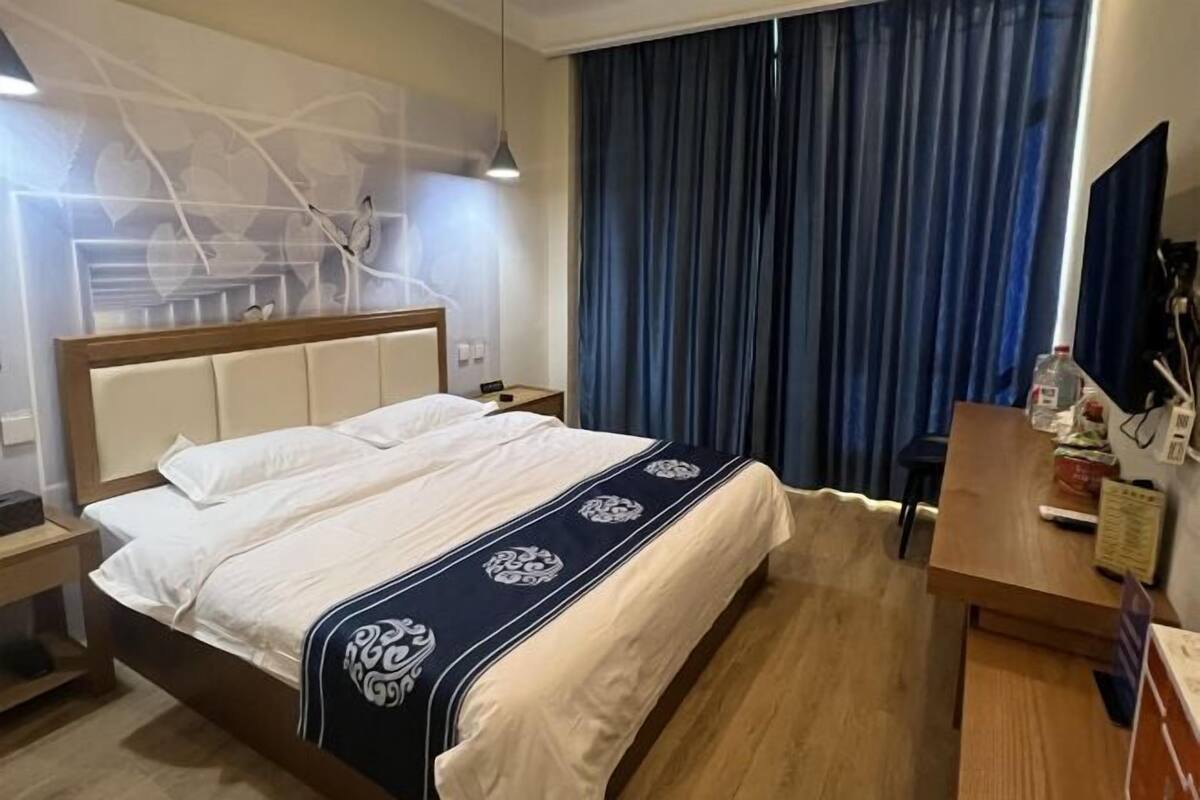 Ein Hotelzimmer mit Bett, Schreibtisch, Stuhl, Fernseher und einem Fenster mit Vorhängen.