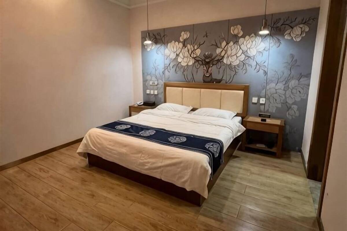 Ein Schlafzimmer mit Bett, Nachttischen, einer Wandlampe und einer floralen Wandmalerei.