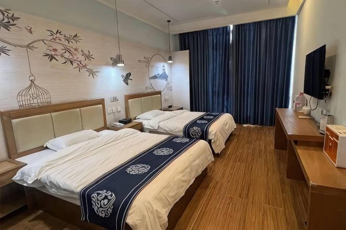 Ein Hotelzimmer mit zwei Betten, Holzboden, Schreibtisch, Fernseher und einem Fenster mit Vorhängen.