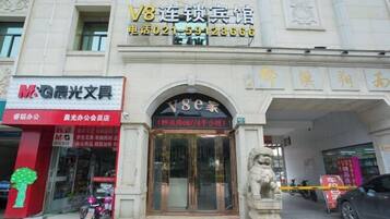 A building with a storefront labeled "V8连锁宾馆" and a phone number.