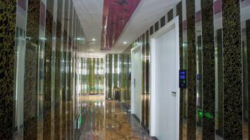 A hallway with reflective walls and a marble floor, leading to a door with a digital display.
