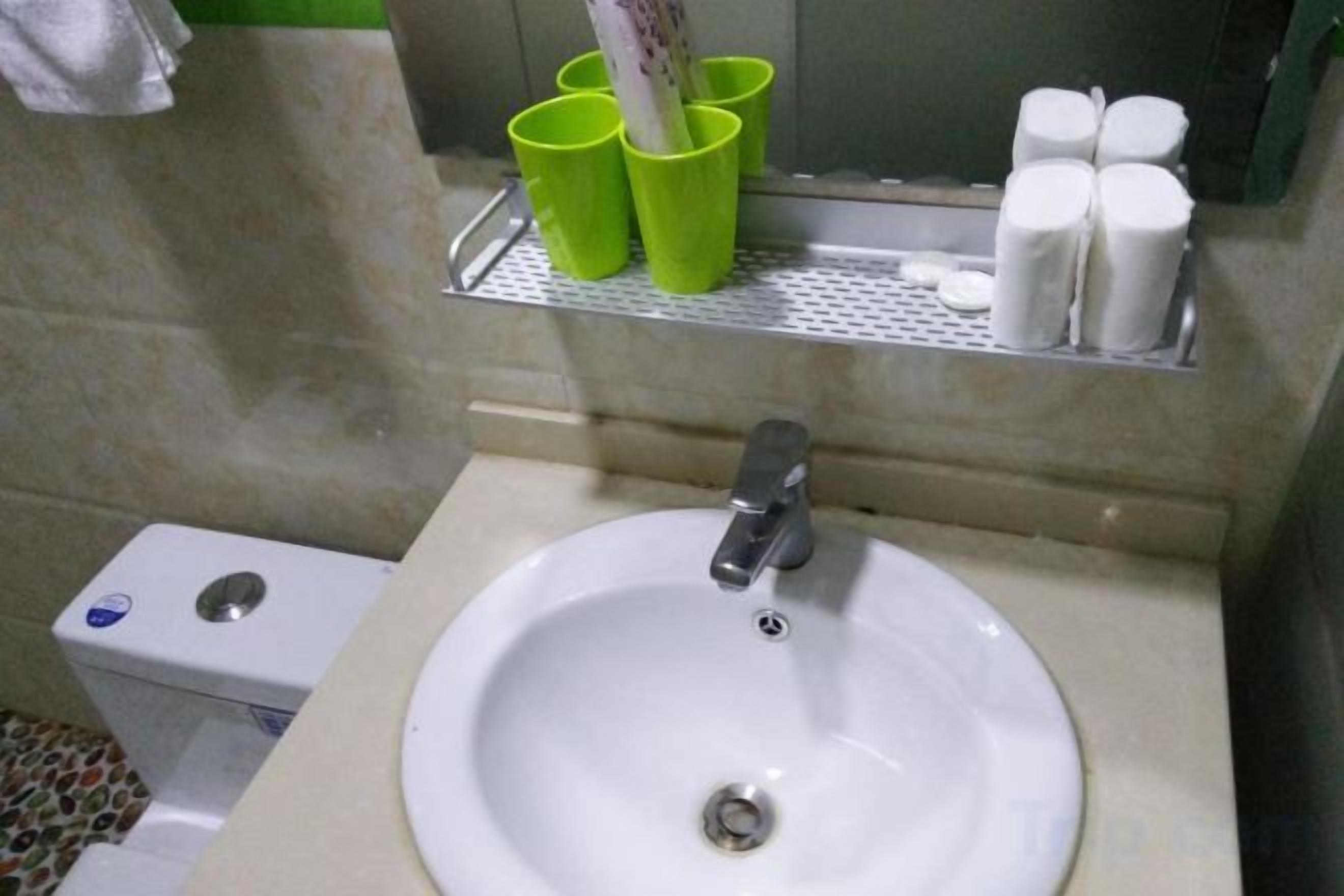 Et badeværelse med håndvask, toilet og grønne kopper på en hylde.