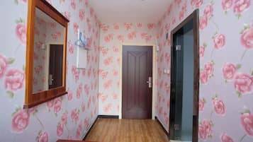A hallway with floral wallpaper, a wooden door, and a mirror on the left wall.