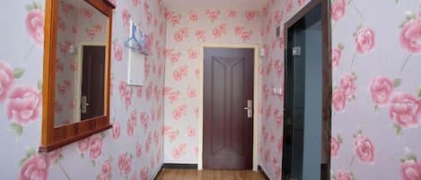 A hallway with floral wallpaper, a wooden door, and a mirror on the left wall.