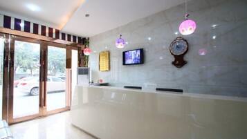 A hotel reception area with a marble counter, a television, and decorative wall clocks.