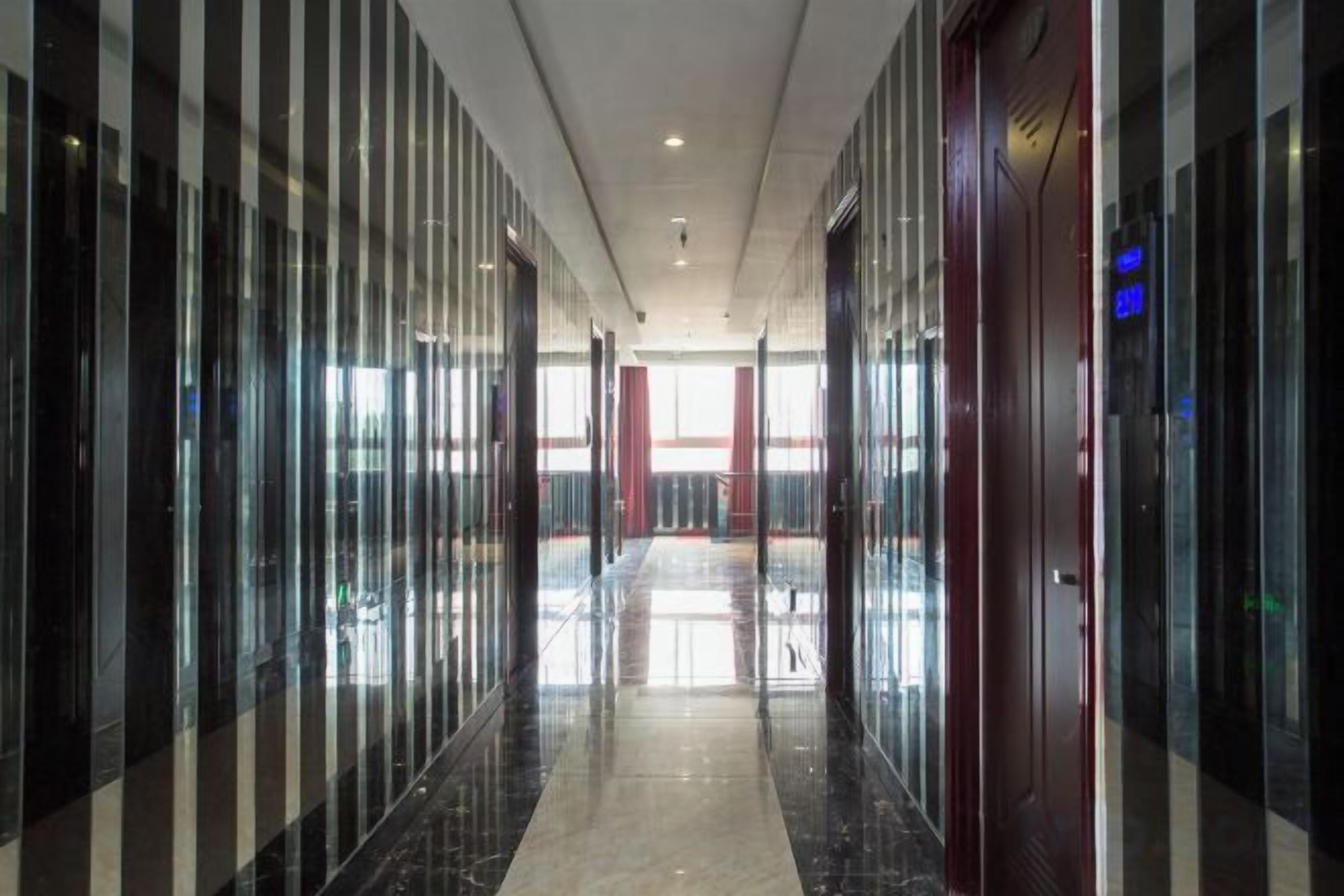 A corridor with reflective floors and glass walls, leading to a red door with a sign.