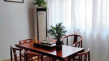 Uma área de refeições com uma mesa de madeira, quatro cadeiras, uma planta em vaso e um eletrodoméstico alto.