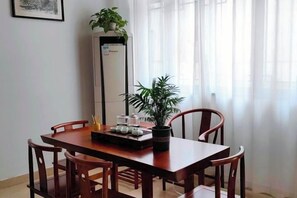 Uma área de refeições com uma mesa de madeira, quatro cadeiras, uma planta em vaso e um eletrodoméstico alto.